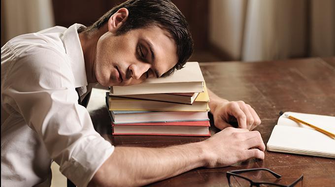 Mann ist über einem Stapel Bücher eingeschlafen und träumt